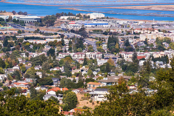 Aerial view of San Carlos in Silicon Valley ; residential areas with houses built on hills in the foreground; industrial areas and the shoreline of San Francisco bay in the background; California
